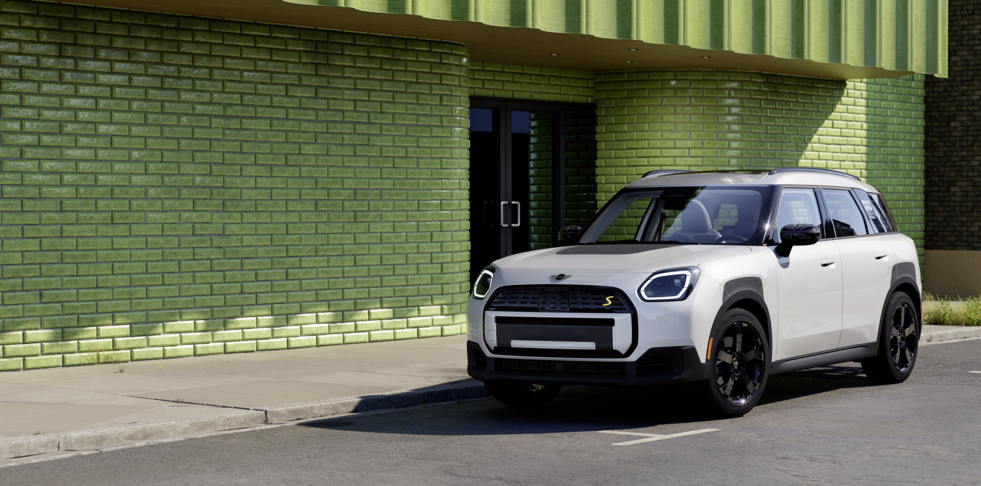 A white MINI Countryman is parked on a city street in front of a building with a bright green facade.